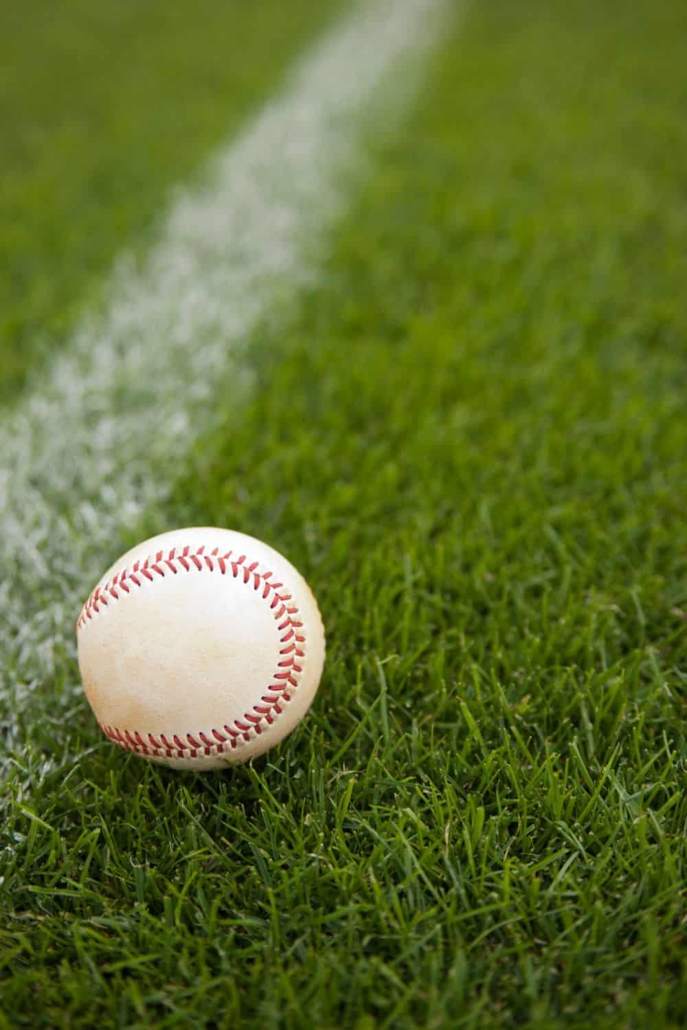 A baseball rests on green Sports Turf near a white foul line on the field.